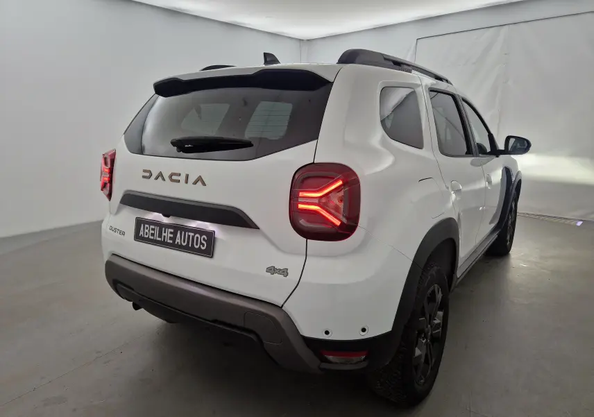 Vue 3/4 arrière droite du Dacia Duster blanc 4x4 2024 avec feux arrière allumés et badge 4x4 visible.