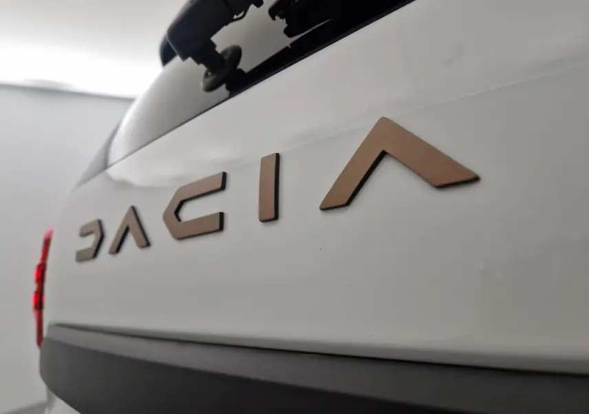 Gros plan sur le logo Dacia en relief bronze sur la partie arrière blanche du Duster 2024, avec feu arrière rouge partiel visible.