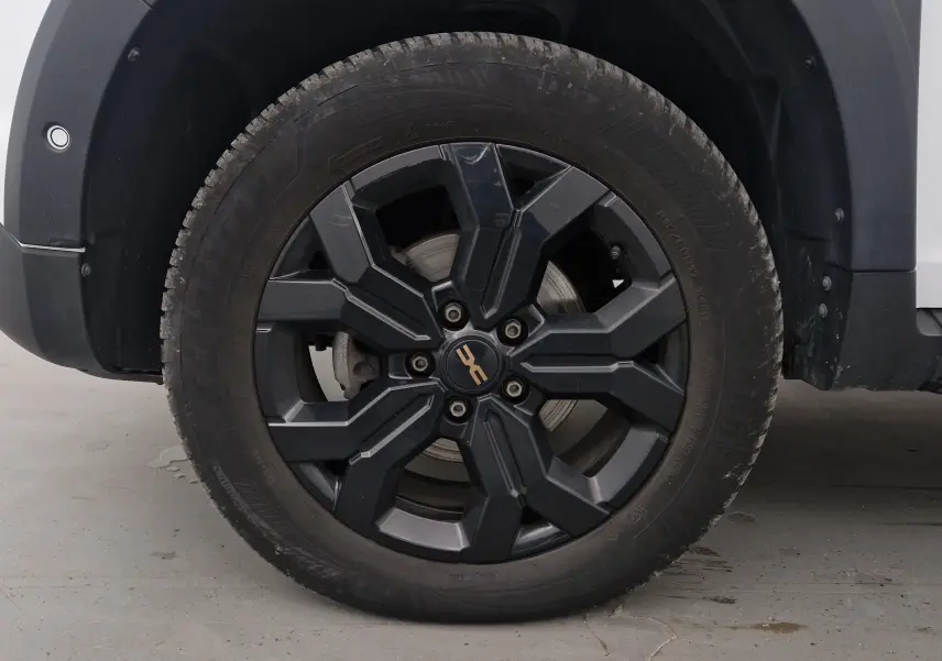 Gros plan sur la roue avant gauche du Dacia Duster blanc 2024, avec jante noire au design robuste et logo central doré.