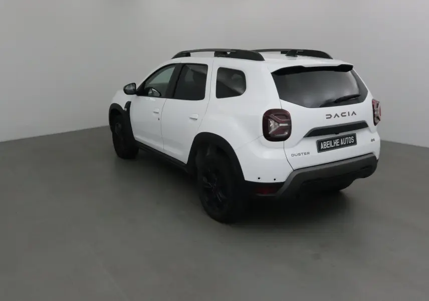 Vue 3/4 arrière droite du Dacia Duster 2024 blanc avec jantes noires et barres de toit noires dans un studio.