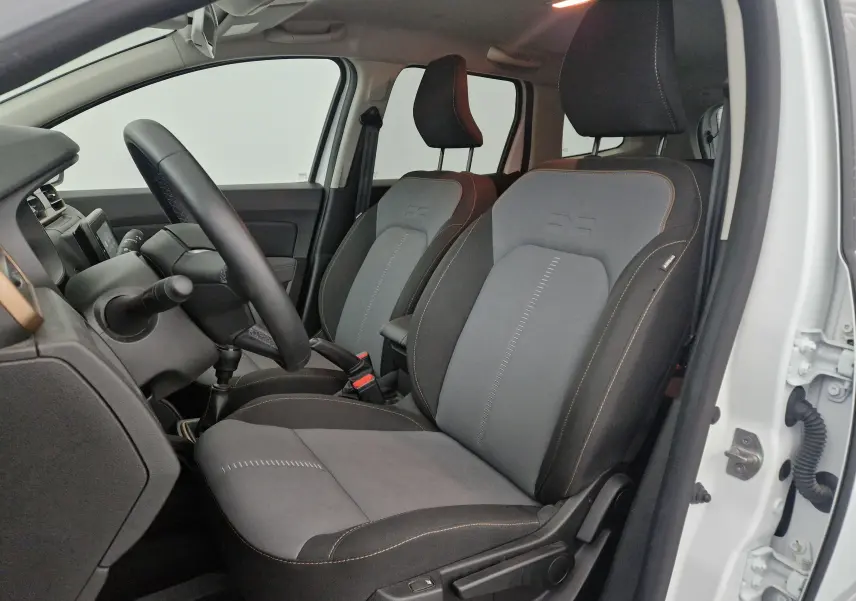 Vue intérieure côté conducteur du Dacia Duster blanc 2024, mettant en valeur les sièges bi-matière gris et noirs avec surpiqûres contrastées.