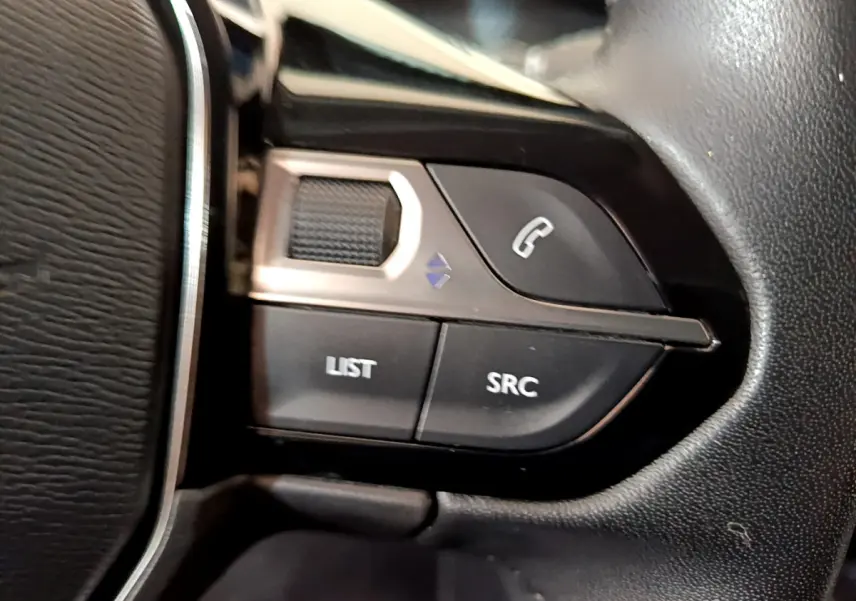 Gros plan sur les commandes du volant cuir noir du Peugeot 2008 gris clair, boutons appel et source audio visibles.