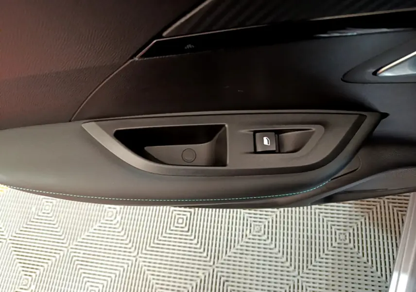 Poignée intérieure et commande de vitre côté gauche en plastique noir dans une Peugeot 2008 gris clair 2021.