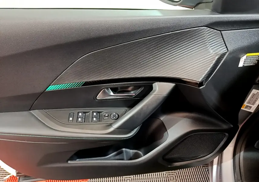 Vue rapprochée de la porte côté conducteur du Peugeot 2008 gris clair, avec insert imitation carbone et commandes électriques.