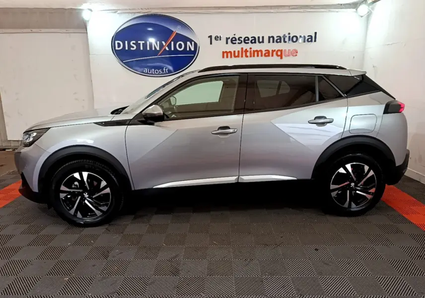 Profil côté gauche d'un Peugeot 2008 gris clair 2021 dans un showroom avec logo Distinxion en arrière-plan.