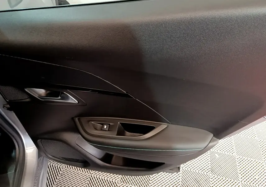 Gros plan sur la porte côté gauche du Peugeot 2008 gris clair, montrant la poignée et les commandes de vitre.