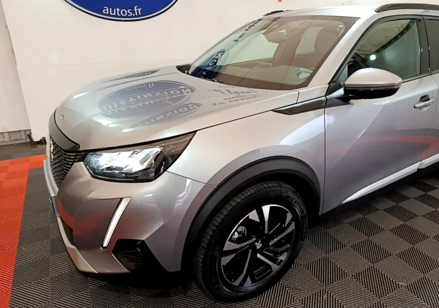 Peugeot 2008 gris clair vue 3/4 avant droit, mettant en valeur ses phares LED et jantes noires modernes.