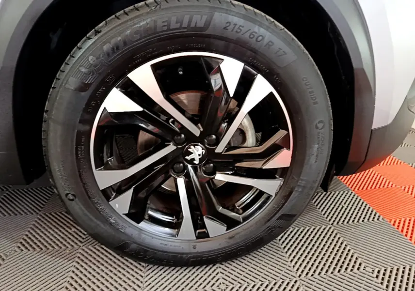 Gros plan sur la roue avant droite du Peugeot 2008 gris clair, jante alliage noire et argentée au design moderne.