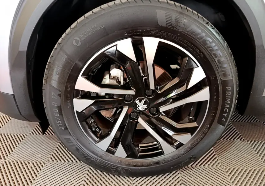 Gros plan sur la roue avant droite du Peugeot 2008 gris clair, jante alliage noire et argent avec logo lion central.