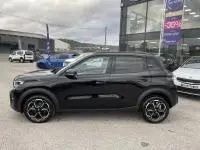 Vue de profil côté gauche d'une Citroën C3 1.2 turbo noire 2025 avec jantes noires, stationnée devant un showroom.