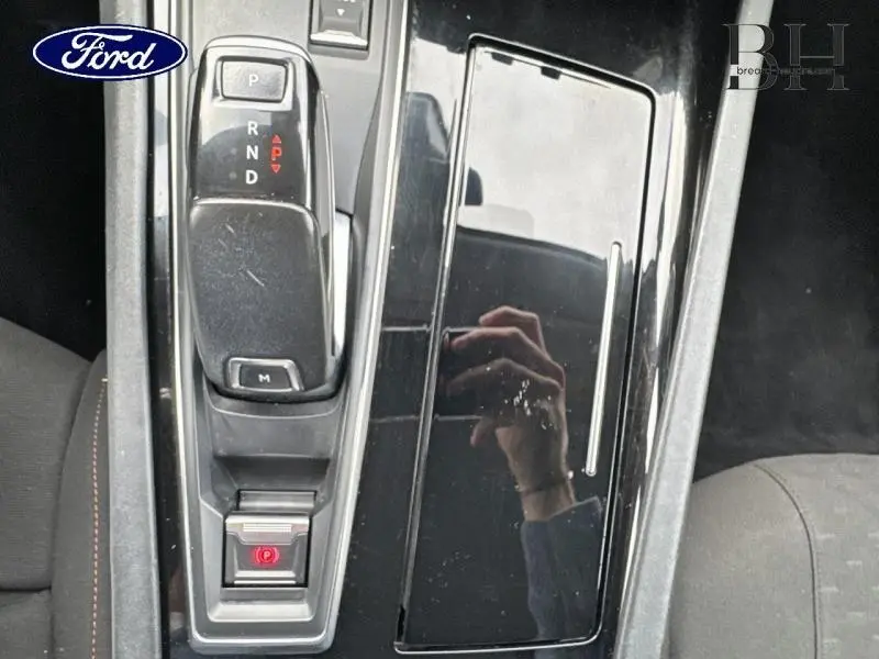 Gros plan sur la console centrale noire brillante avec levier de vitesse automatique et frein à main électrique.