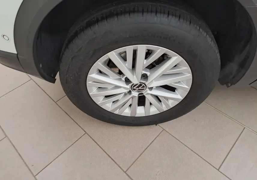 Gros plan sur la roue avant gauche du Volkswagen T-Roc blanc toit noir, mettant en valeur la jante argentée à design multiple.