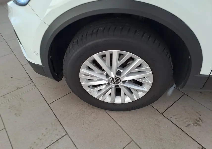 Gros plan sur la roue avant gauche du Volkswagen T-Roc blanc pur avec jante alliage et toit noir visible en partie.
