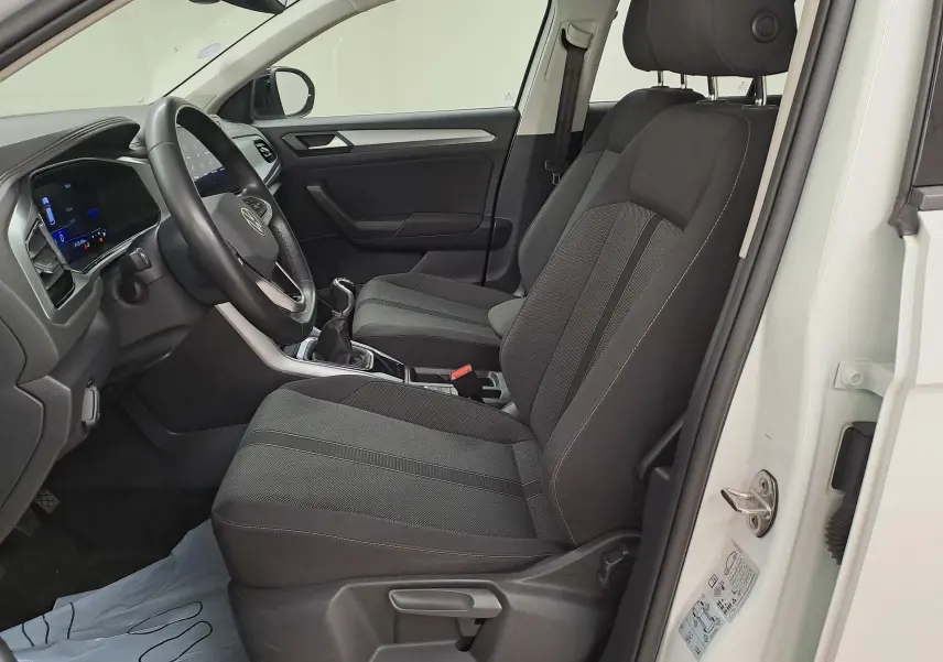 Vue intérieure côté conducteur du Volkswagen T-Roc blanc toit noir, montrant les sièges noirs et la console avec boîte manuelle.