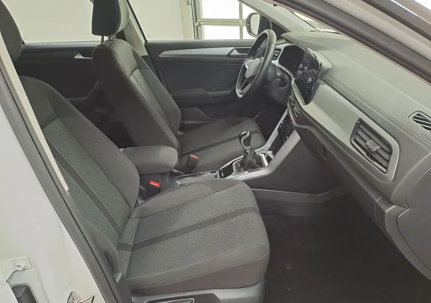 Vue intérieure côté conducteur du Volkswagen T-Roc 2022 blanc, montrant les sièges noirs et la console avec boîte manuelle.