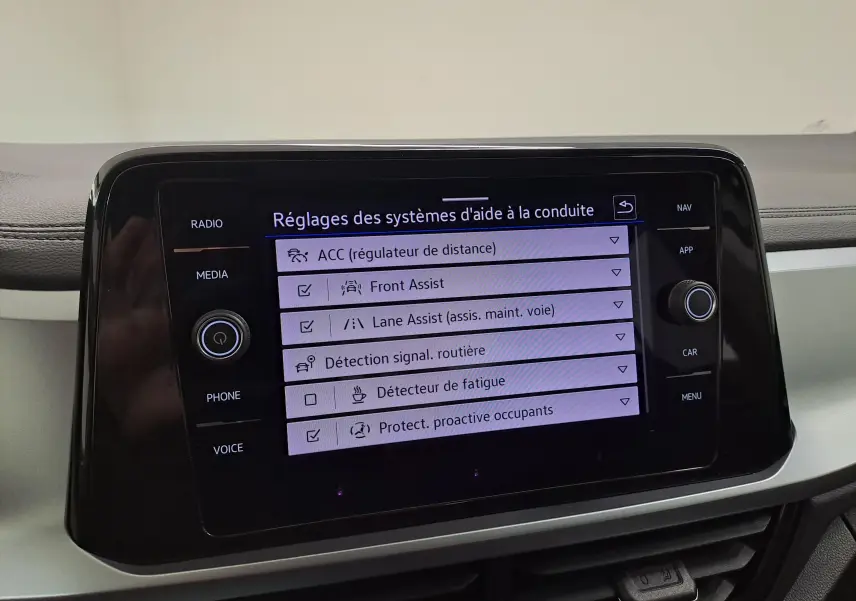 Vue de face de l'écran tactile du Volkswagen T-Roc blanc toit noir, affichant les réglages des aides à la conduite.