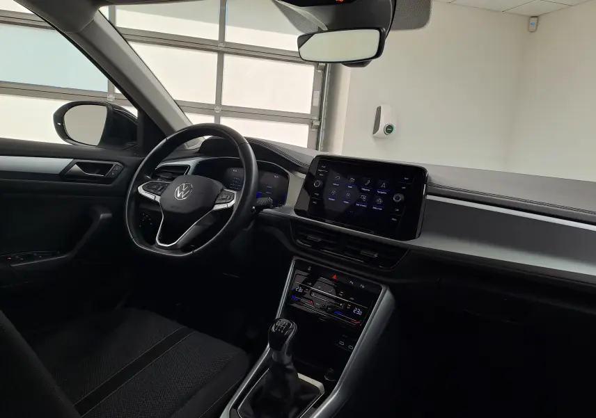 Vue intérieure côté conducteur du Volkswagen T-Roc 2022, tableau de bord noir avec écran tactile et levier de vitesses manuel.