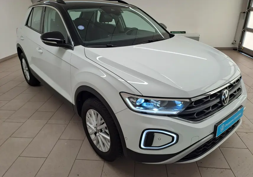 Volkswagen T-Roc blanc pur avec toit noir, vue 3/4 avant droit, phares et feux LED allumés en intérieur.