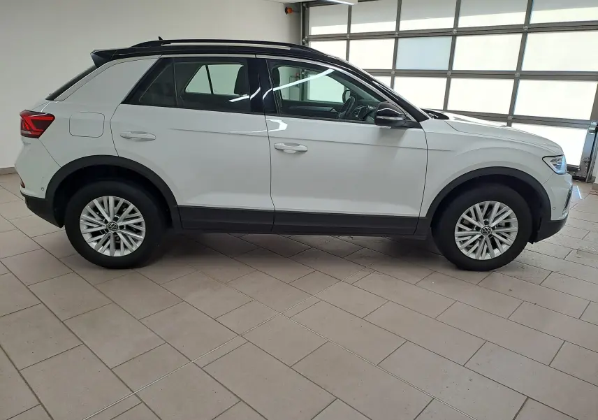 Vue de profil côté gauche du Volkswagen T-Roc blanc pur avec toit noir, jantes alliage et détails noirs contrastants.