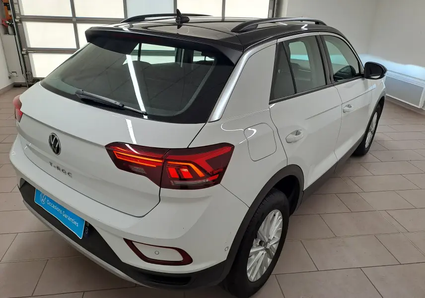 Vue 3/4 arrière droite du Volkswagen T-Roc blanc pur avec toit noir, feux arrière allumés, en intérieur showroom.