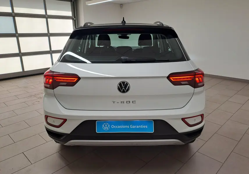 Vue arrière d'un Volkswagen T-Roc blanc pur avec toit noir, feux allumés, dans un garage lumineux.