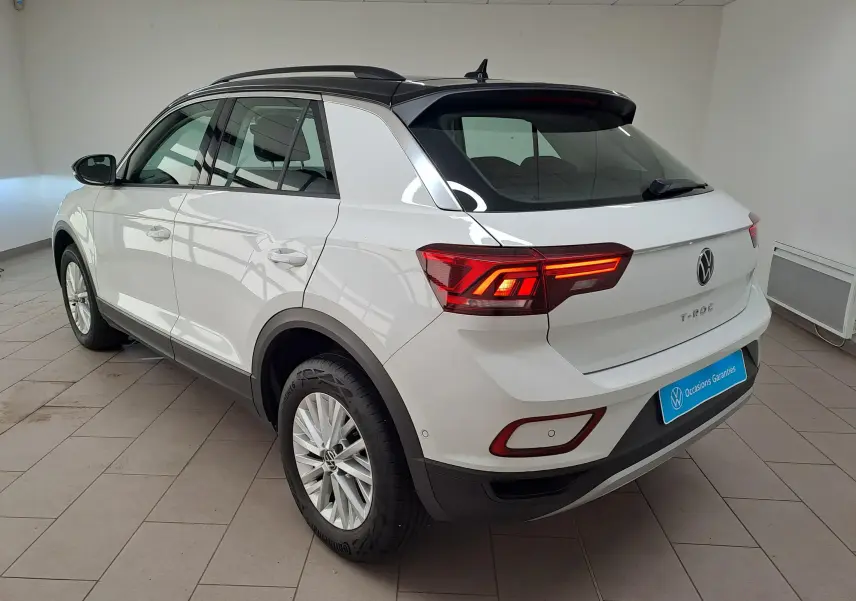 Vue 3/4 arrière droite du Volkswagen T-Roc blanc toit noir, avec feux arrière allumés dans un showroom.