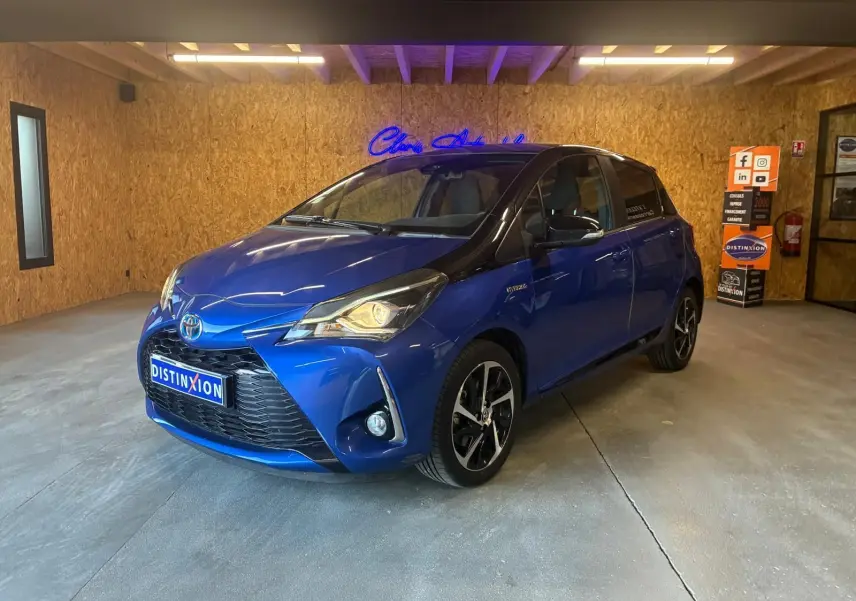 Toyota Yaris hybride bleu en 3/4 avant droit, avec jantes noires et toit noir dans un garage intérieur.