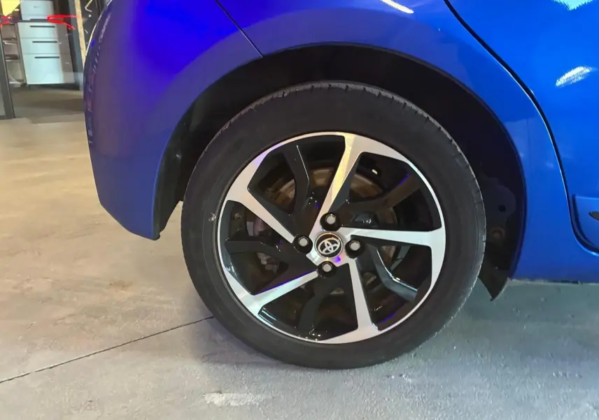 Gros plan sur la roue arrière droite d'une Toyota Yaris bleu vif avec jante alliage bicolore en intérieur d'atelier.
