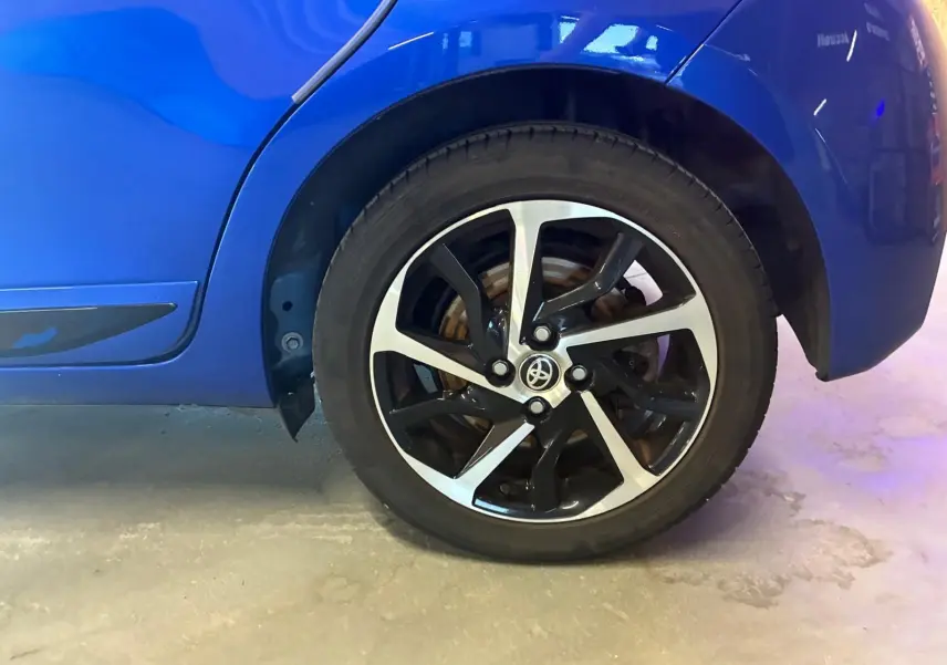 Gros plan sur la roue arrière droite d'une Toyota Yaris hybride bleue, mettant en valeur la jante alliage bicolore.