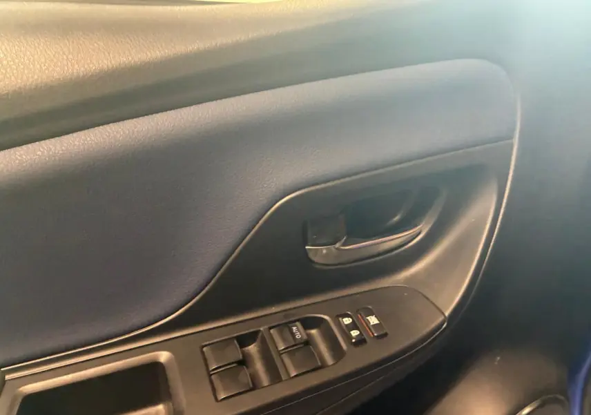 Gros plan sur la porte intérieure côté conducteur de la Toyota Yaris bleu, montrant les commandes des vitres et la poignée noire.