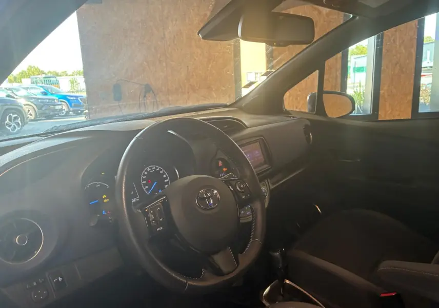 Vue intérieure côté conducteur de la Toyota Yaris hybride 2020, volant cuir noir et tableau de bord avec écran tactile.