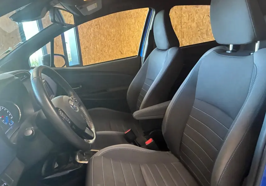 Vue intérieure côté conducteur de la Toyota Yaris hybride 2020, sièges tissu noir et volant multifonction.