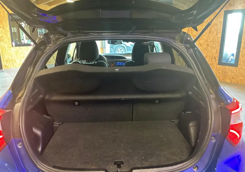 Vue arrière ouverte du coffre d’une Toyota Yaris hybride bleue 2020, intérieur noir et tablette de coffre visible.