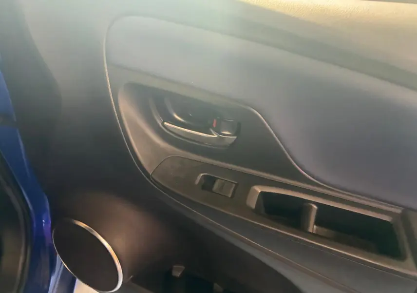 Vue intérieure du panneau de porte côté gauche d'une Toyota Yaris hybride bleue avec commande de vitre et poignée noire.