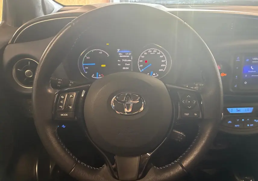 Vue rapprochée du volant noir de la Toyota Yaris hybride 2020 avec tableau de bord et écran tactile visibles.