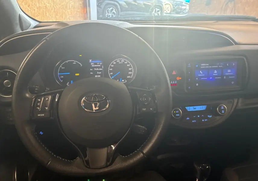 Vue intérieure centrée sur le volant de la Toyota Yaris hybride 2020 avec tableau de bord et écran tactile allumé.