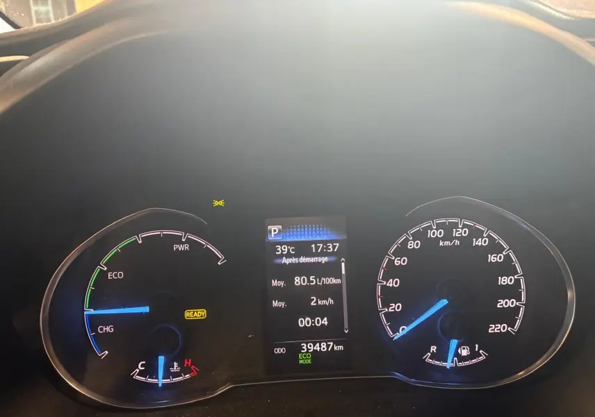 Vue rapprochée du tableau de bord numérique d'une Toyota Yaris hybride bleue, affichant la vitesse, la température et l'autonomie.