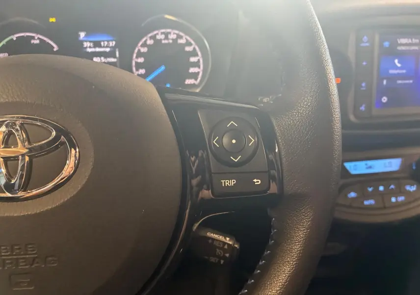 Gros plan sur le volant noir de la Toyota Yaris 2020 avec commandes multifonctions et tableau de bord lumineux en arrière-plan.