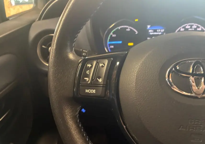 Gros plan sur le volant noir de la Toyota Yaris 2020 avec commandes intégrées et tableau de bord hybride en arrière-plan.