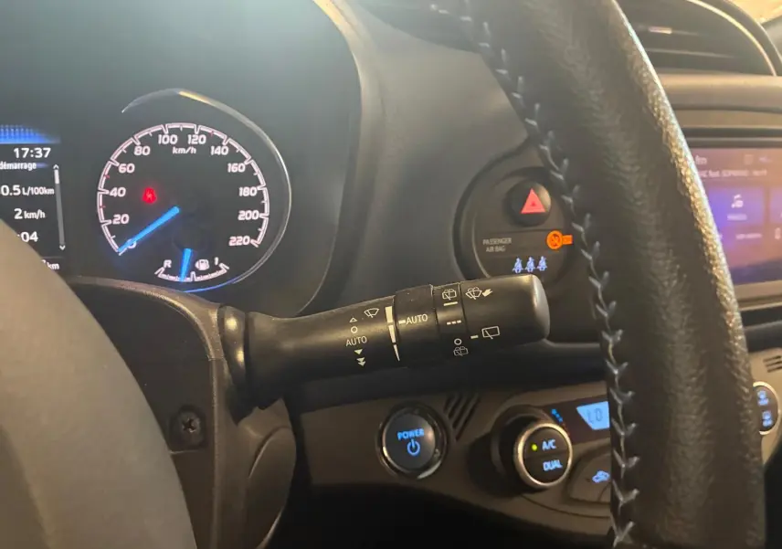 Vue intérieure centrée sur le combiné d'instruments et le commodo d'essuie-glace d'une Toyota Yaris hybride bleue de 2020.