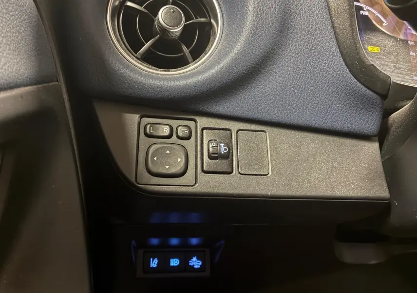 Détail intérieur côté gauche du tableau de bord bleu de la Toyota Yaris 2020, avec commandes des rétroviseurs et réglage des phares.