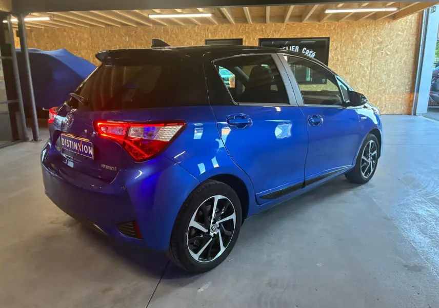 Vue 3/4 arrière droite d'une Toyota Yaris hybride bleue 5 portes avec jantes alliage et vitres teintées, stationnée en intérieur.