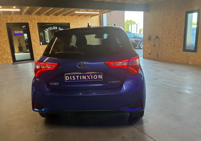 Vue arrière d'une Toyota Yaris hybride bleue 2020, avec feux arrière allumés dans un garage lumineux.