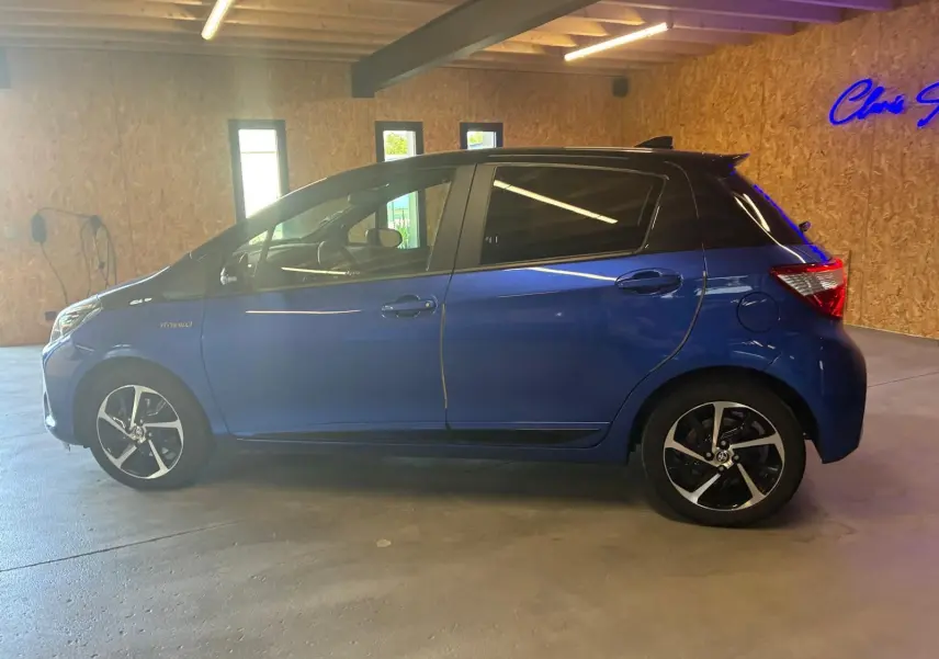 Profil côté gauche de la Toyota Yaris hybride bleue 5 portes, avec toit noir et jantes alliage distinctives.