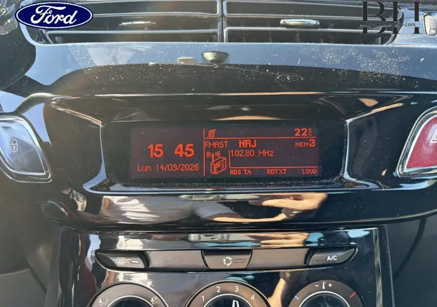Gros plan sur la console centrale noire brillante de la Citroën DS3 rouge Rubi, affichant l’horloge et la radio FM.