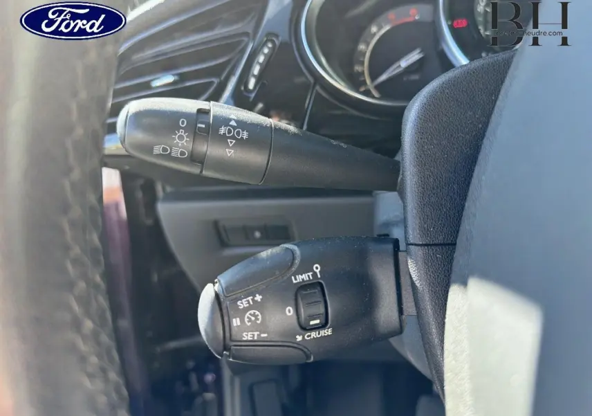 Gros plan sur la commande de régulateur de vitesse et des feux, intérieur noir du volant d'une Citroën DS3 rouge Rubi.