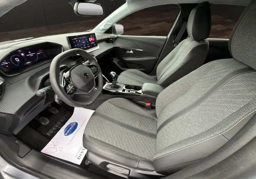 Vue intérieure côté conducteur de la Peugeot 208 gris clair, volant cuir multifonctions et sièges tissu gris avec surpiqûres.