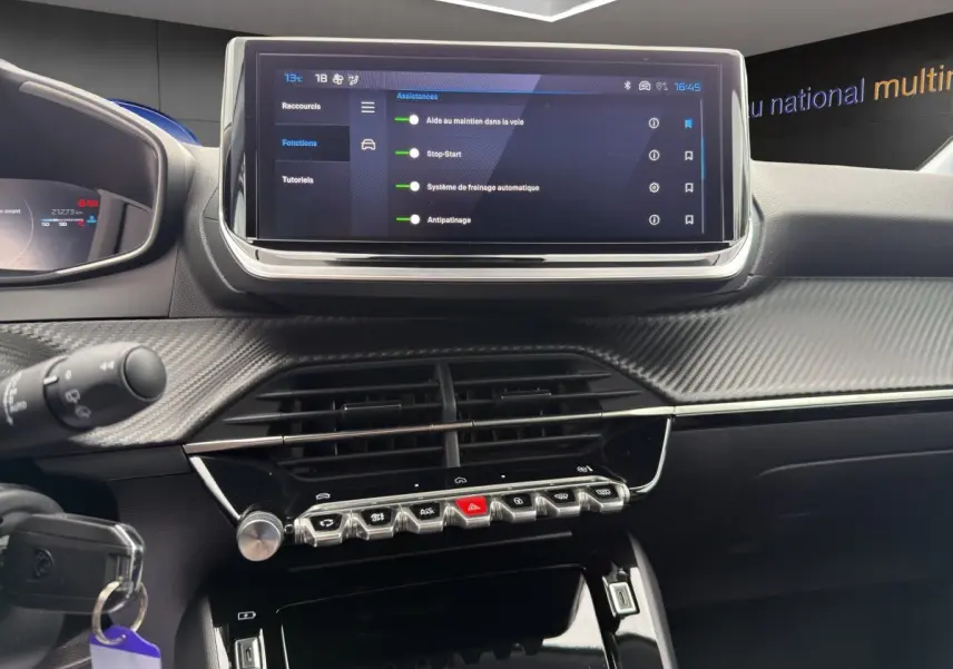 Vue rapprochée du tableau de bord noir et carbone de la Peugeot 208 2025 avec écran tactile central et commandes piano.