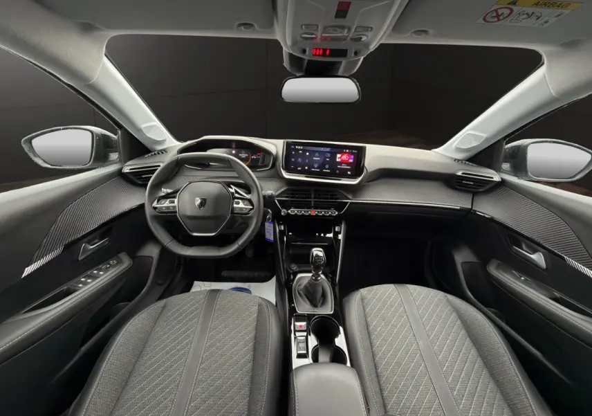 Vue intérieure avant de la Peugeot 208 2025 gris clair, volant cuir multifonctions et écran tactile central visible.
