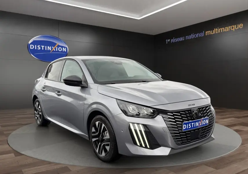 Peugeot 208 gris clair vue 3/4 avant droit, avec calandre distinctive et feux LED verticaux allumés.